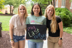 Three students pose with a chalkboard that says "My Last First Day"