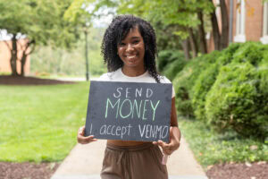 A student poses with a chalkboard that says "Send money. I accept Venmo." 