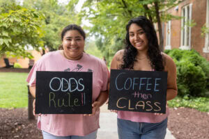 Two students pose together holding chalkboards with funny sayings on them
