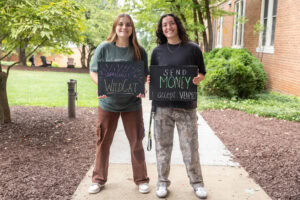 Two students pose together holding chalkboards with funny sayings on them