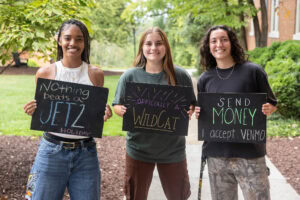 A group of students pose together holding chalkboards with funny sayings on them