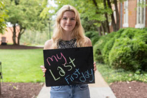 A student poses with a chalkboard that says "My Last First Day"