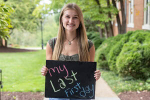 A student poses with a chalkboard that says "My Last First Day"