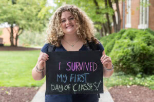 A student poses with a sign that says "I survived my first day of classes"