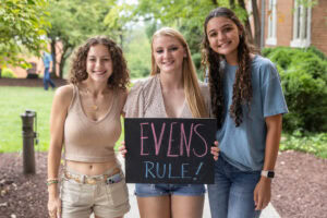 Student pose together with a sign that says "Evens Rule"