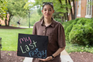 A student poses with a chalkboard that says "My Last First Day"