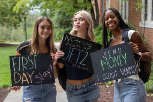 A group of students pose together holding chalkboards with funny sayings on them