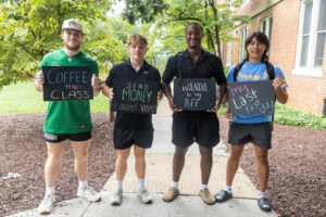 A group of students pose together holding chalkboards with funny sayings on them