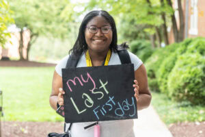 A student poses with a chalkboard that says "My Last First Day" 