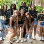 A group of students pose together holding chalkboards with funny sayings on them