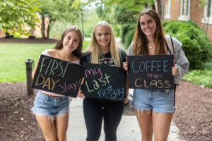 A group of students pose together holding chalkboards with funny sayings on them