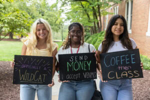 A group of students pose together holding chalkboards with funny sayings on them