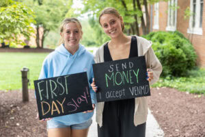 Two students pose together with chalkboards that say "first day slay" and "send money" 