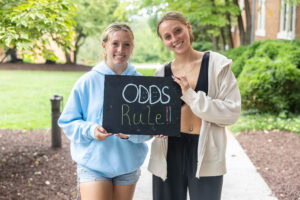 Two students pose with a chalkboard that says "Odds Rule" 