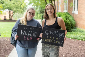 Two students pose together holding chalkboards with funny sayings on them