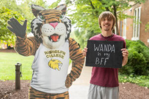 A student poses with a chalkboard that says "Wanda is my BFF" next to a cardboard cutout of the Wanda WildCat mascot