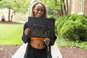 A student poses with a chalkboard that says "Officially a WildCat"