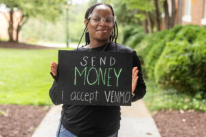 A student poses with a chalkboard that says "Send money. I accept Venmo." 