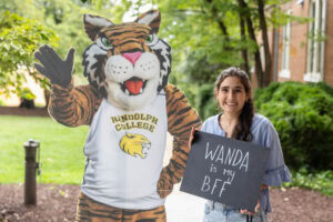 A student poses with a chalkboard that says "Wanda is my BFF" next to a cardboard cutout of the Wanda WildCat mascot