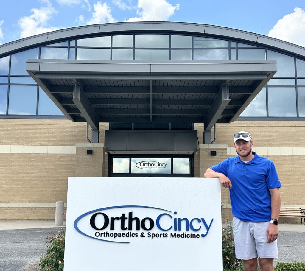A man stands next to a sign for OrthoCincy 