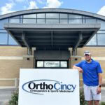 A man stands next to a sign for OrthoCincy