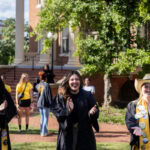 Three students walk on campus clapping their hands