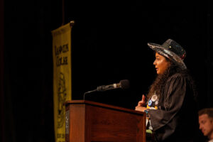 A student stands at a podium, wearing her graduation gown