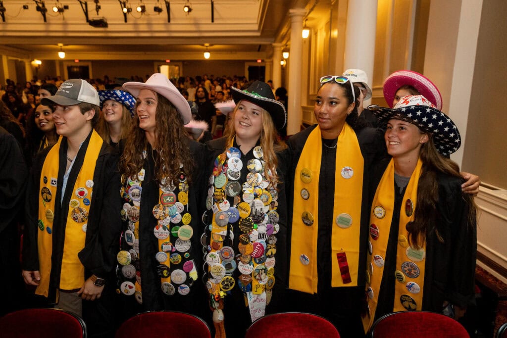 Students stand arm in arm in an auditorium 