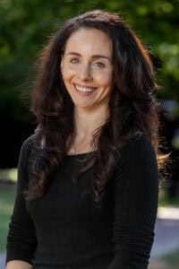 A woman poses for a photo in front of trees 