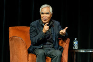 Nick Ut speaks onstage, sitting in an orange chair