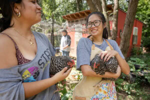 Two students smile at each other while holding chickens