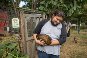 A male student looks down at the chicken he is holding in a garden