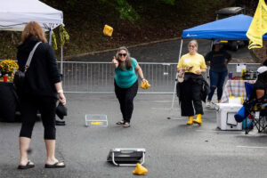 A woman throws a bean bag during a game of cornhole, while other participants look on