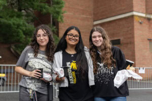 Three women pose for a photo together while holding food 