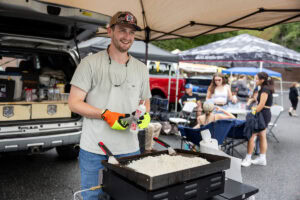 A man smiles while standing at a grill, cooking rice 