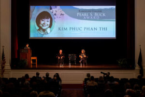A far away shot of the stage in Smith Hall Theatre, with a projection in the background with Kim Phuc Phan Thi's name on it