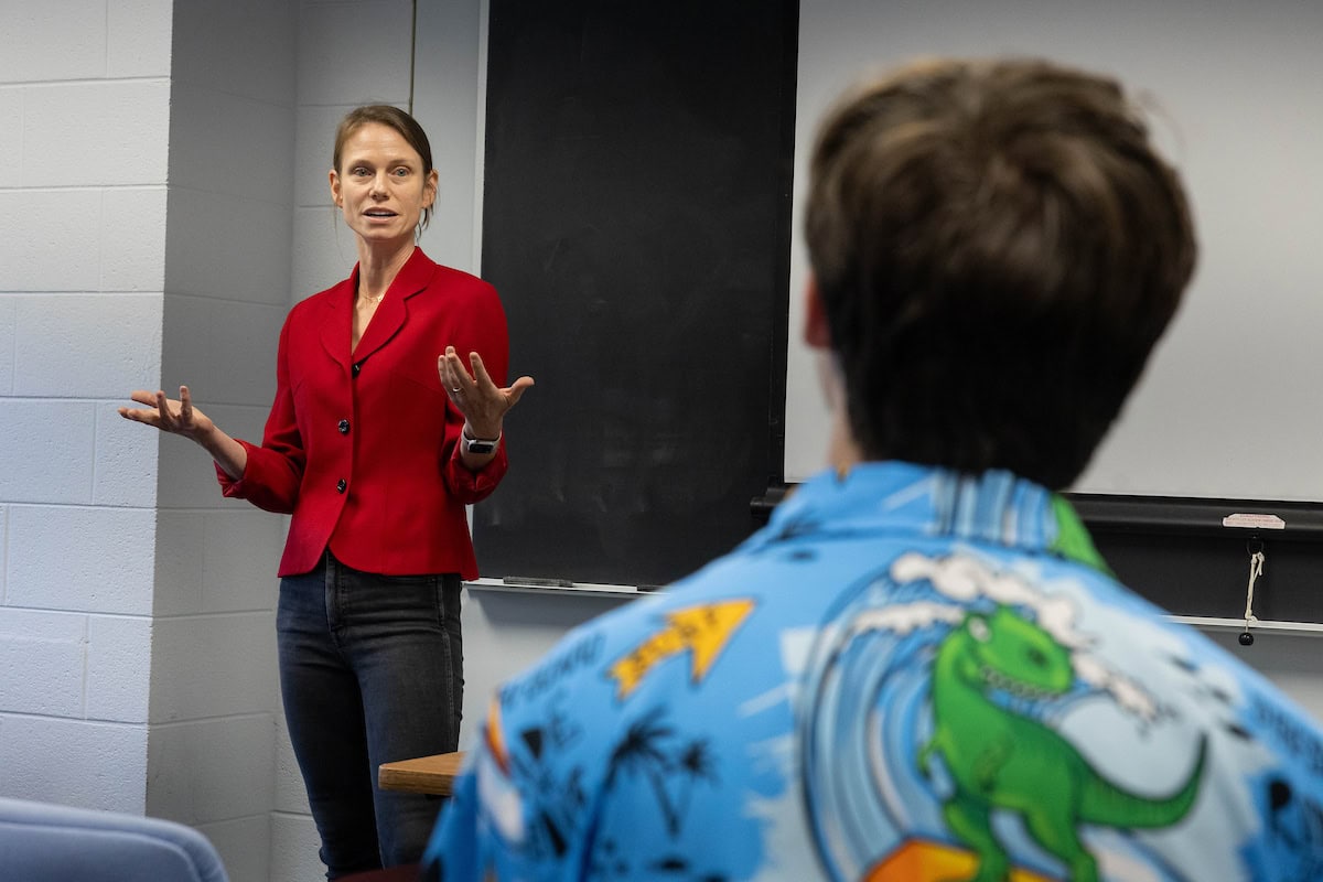 A woman stands in front of a classroom, speaking 