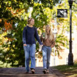 Two female students walk together on a brick pathway, with beautiful trees in the background Two female students walk together on a brick pathway, with beautiful trees in the background