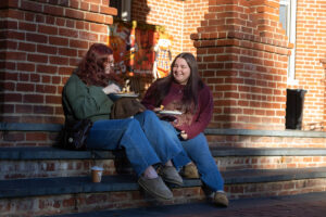 Two students sit on a set of brick steps, in front of a building, with plates of food