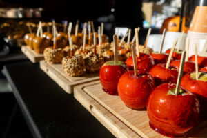 A table full of candy apples, some just dipped in caramel and others with candy on them