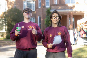 Two students pose for the camera with funny glasses on, one holding some cotton candy