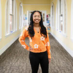 A student stands in a hallway, smiling for a photo