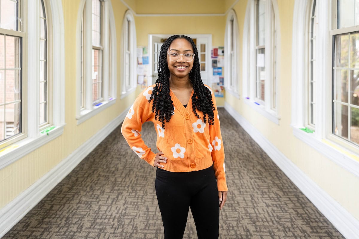 A student stands in a hallway, smiling for a photo