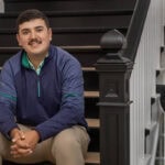 A male student sits on a set of steps, smiling for the camera