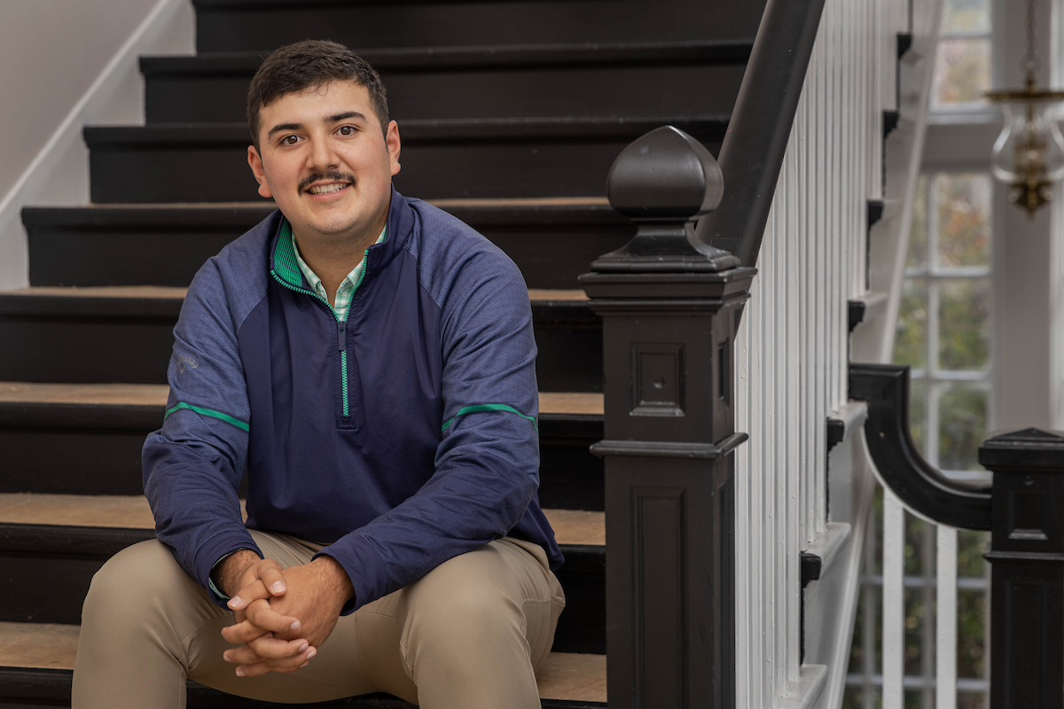 A male student sits on a set of steps, smiling for the camera