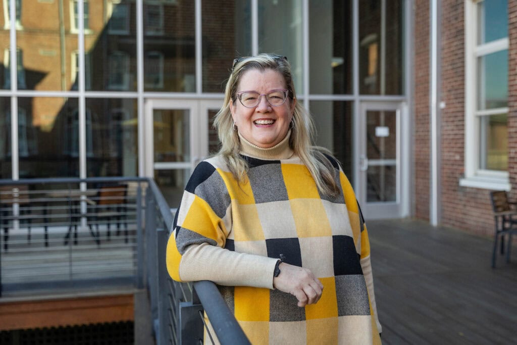 A woman poses for a photo, leaning on a railing outside of a building