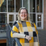 A woman poses for a photo, leaning on a railing outside of a building