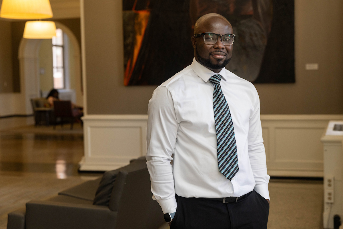 A man poses for a photo, wearing a tie and white shirt, with his hands in his pockets