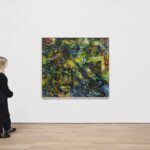 A woman stands in gallery looking at a large painting A woman stands in gallery looking at a large painting