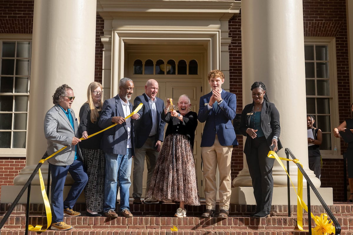 A group of people claps and cheers after cutting a ribbon in front of a building 